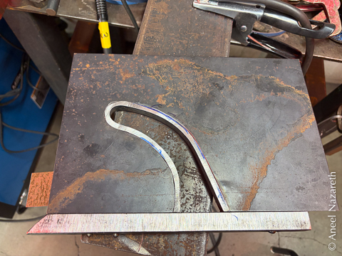 The front view of the finished piece. The sheet metal (dark and rusty) contrasts with the bar and the curve (shiny and still quite phallic)